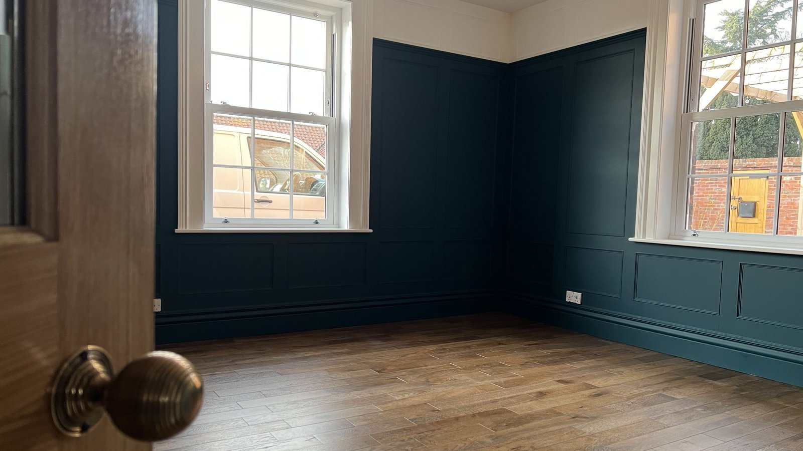 A panelled reception room finished in deep teal with restored sash windows and an oak floor