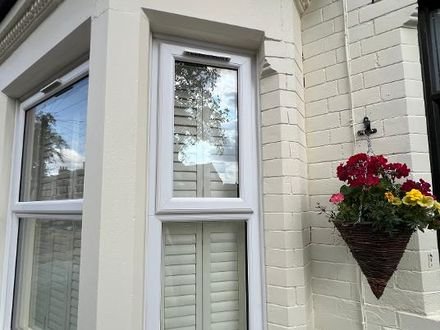 A bay window with its render and brickwork painted cream beneath a dentil cornice