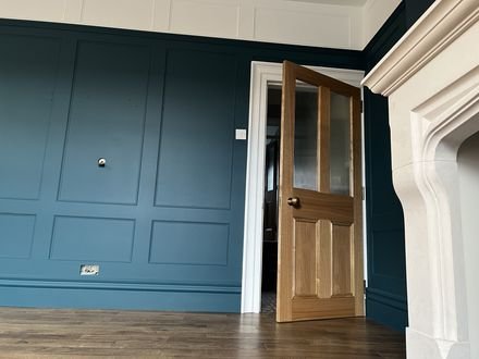 A reception room in deep teal panelling with an oak door and stone fireplace