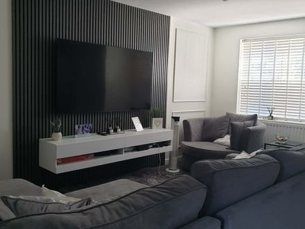 A living room with dark vertical slat panelling behind the television and white box mouldings around it
