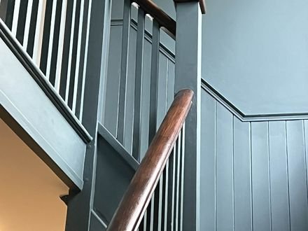 A staircase in green-grey with vertical panelling below a dark timber handrail